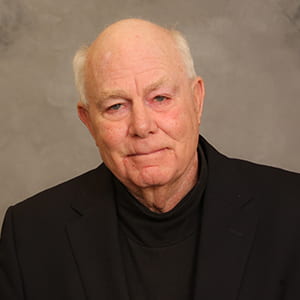 headshot of man in black shirt and black blazer